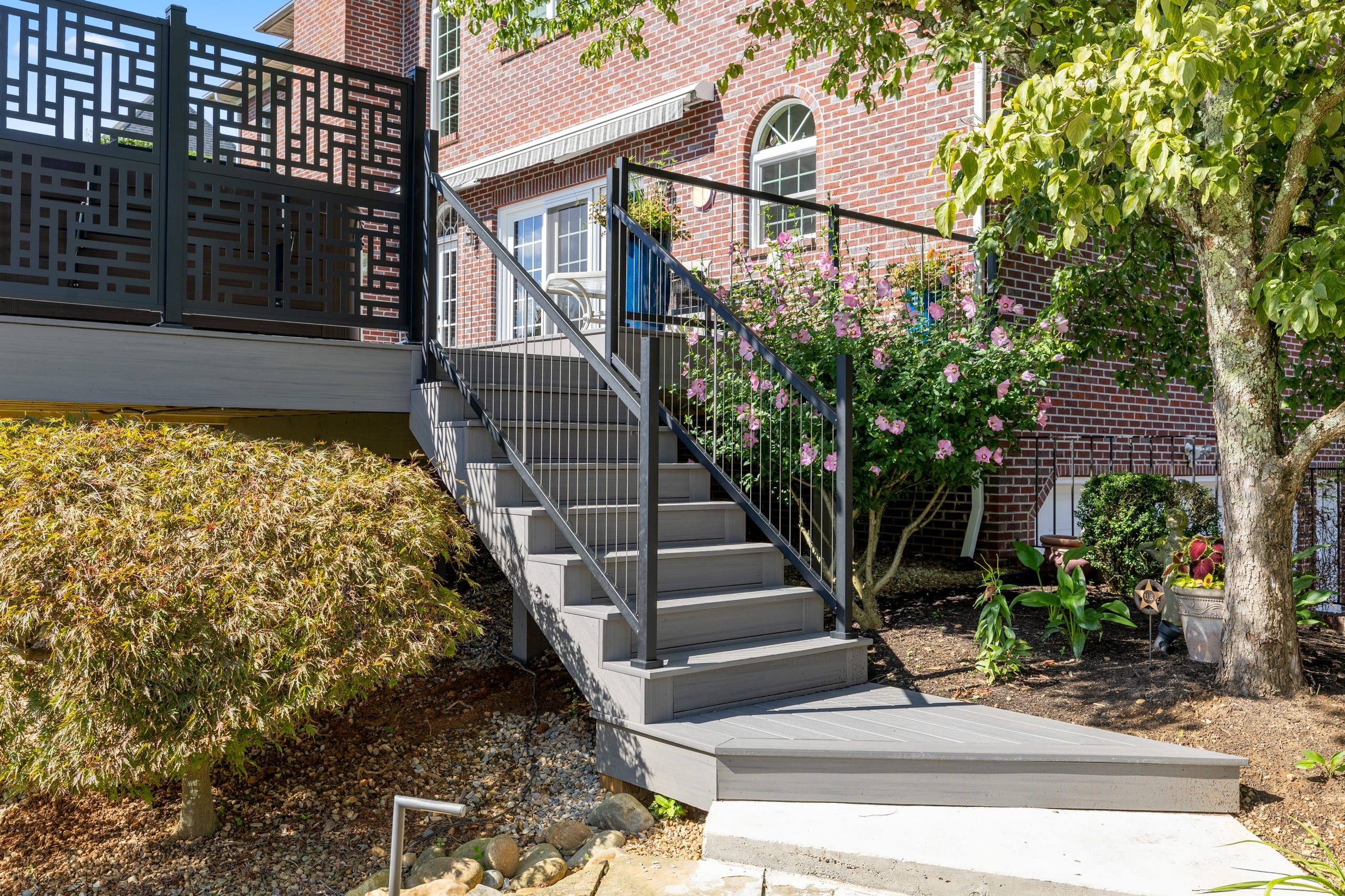 Composite staircase with black cable railing descending from the Wilshire deck through rose beds to a landing at grade